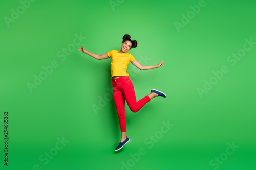 Full length photo of pretty dark skin lady jumping high supporting team at competitions wear casual yellow t-shirt red pants isolated green background