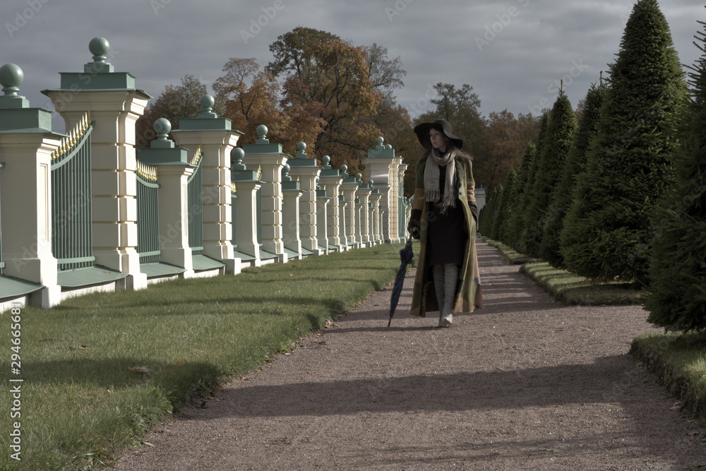 french noir style photo of a young beautiful pretty lady woman posing in a long green and brown dress gown overcoat walks in the garden of the palace in Oranienbaum near Saint Petersburg, Russia