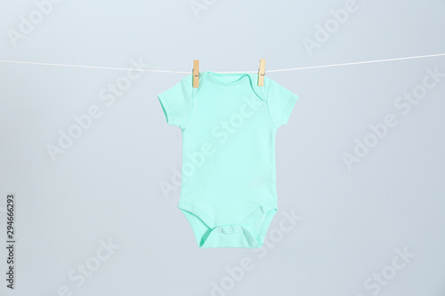 Cute baby onesie hanging on clothes line against light grey background. Laundry day