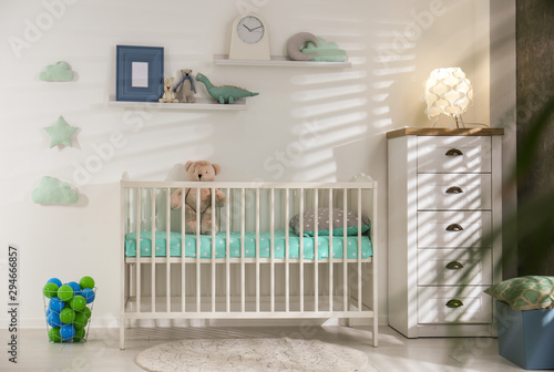 Cute nursery interior with comfortable crib near white wall