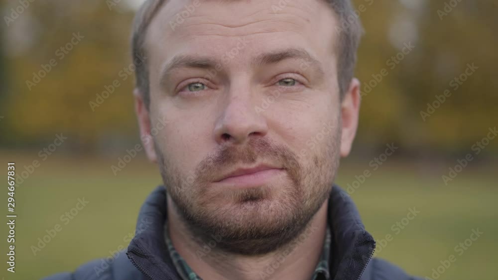 Close-up portrait of an adult caucasian man looking at the camera and making faces. Bearded guy with grey hair and grey eyes standing on the autumn meadow and smiling. Close-up portrait of an adult caucasian man looking at the camera and making faces. Bearded guy with grey hair and grey eyes standing on the autumn meadow and smiling.