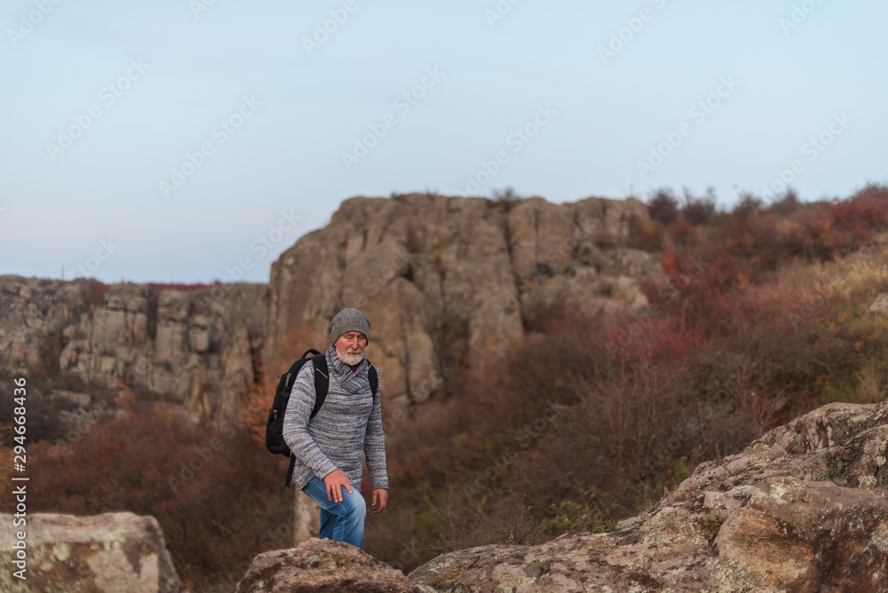 Elder man with gray beard in hat and sweater hiking in canyon