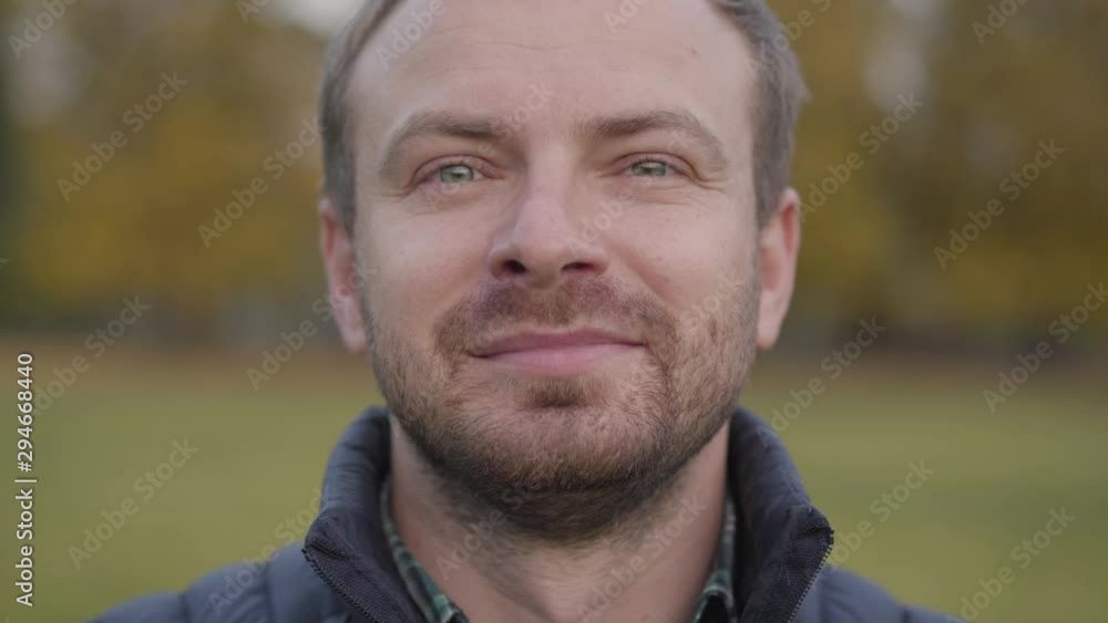 Close-up face of an adult caucasian man looking at the camera and making faces. Bearded guy with grey hair and grey eyes standing on the autumn meadow and smiling. Close-up face of an adult caucasian man looking at the camera and making faces. Bearded guy with grey hair and grey eyes standing on the autumn meadow and smiling.