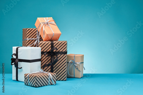 Different sizes, colorful, striped and plain paper gift boxes tied with ribbons and bows on a blue surface and background. Close-up, copy space. photo