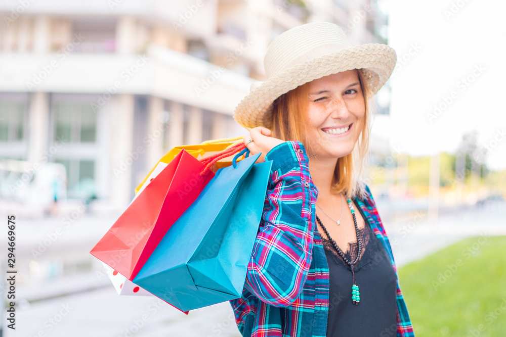 Beautiful girl is holding shopping bags, looking at camera and smiling while walking down the street Beautiful girl is holding shopping bags, looking at camera and smiling while walking down the street