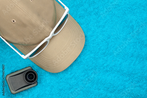 A cap with sunglasses and an action camera lie on a towel.