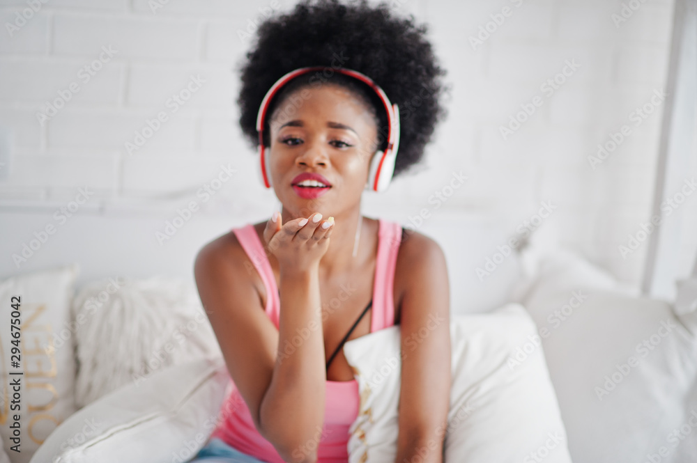 Young african american woman sitting in bed and listen music on earphones. Young african american woman sitting in bed and listen music on earphones.