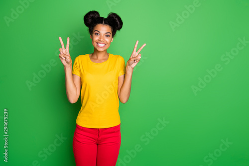Photo of amazing dark skin lady in cool mood showing v-sign symbols wear casual yellow t-shirt and red pants isolated green background