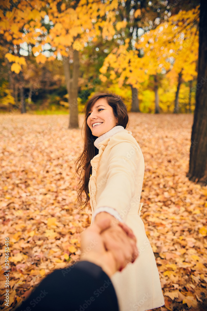 Portrait of happy young woman holding hand and dragging friend in autumn park. Cheerful girl walking with boyfriend at fall. Season, friendship, dating Portrait of happy young woman holding hand and dragging friend in autumn park. Cheerful girl walking with boyfriend at fall. Season, friendship, dating