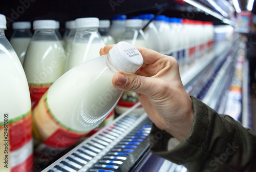 Womans hand holding milk bottle in supermarket. Man shopping milk in grocery store. Man checks product expiration date before buying it. Close-up. photo