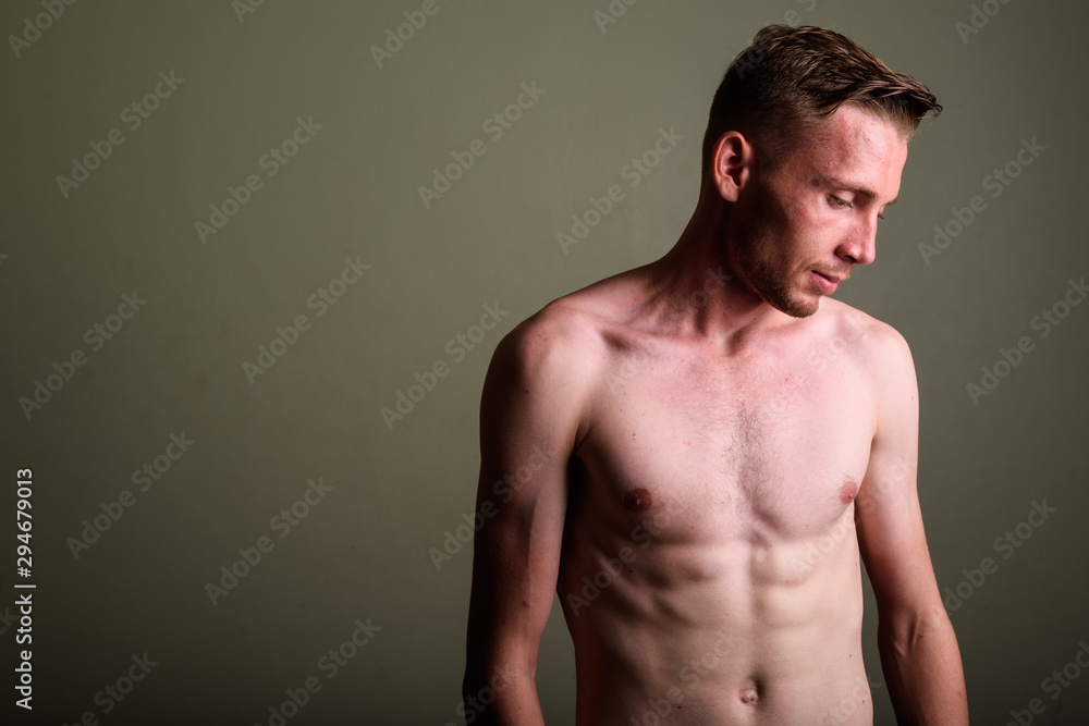 Fototapeta premium Young man shirtless against colored background looking down
