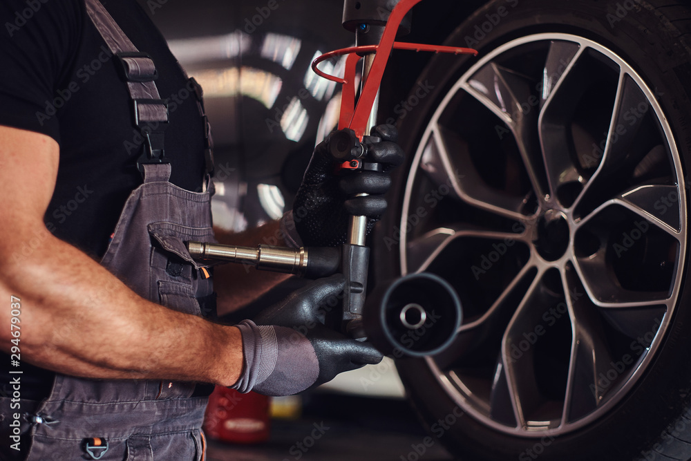 Fototapeta premium Muscular man is fixing car's wheel with special tool at auto service.