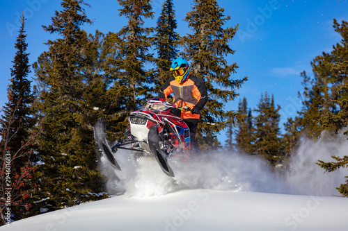 A man is riding snowmobile in mountains. Beautiful morning light. jump on a snow bike. pilot on a sports snowmobile in a mountain forest. The concept of skidooking. Lifestyle is active in winter sport
