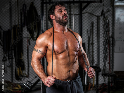 A shirtless, muscular man rests after skipping rope.
