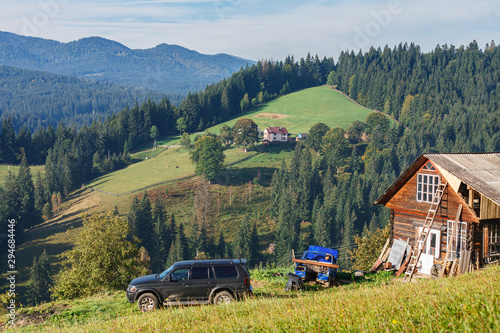 Beautiful mountain landscape with traditional wooden cabins on hill, houses and car in front, colorful view of mountain range in summer day