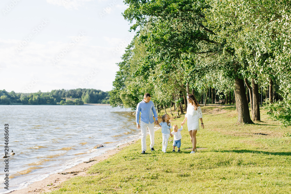 A family with two young children walks along the shore of the lake in the summer A family with two young children walks along the shore of the lake in the summer