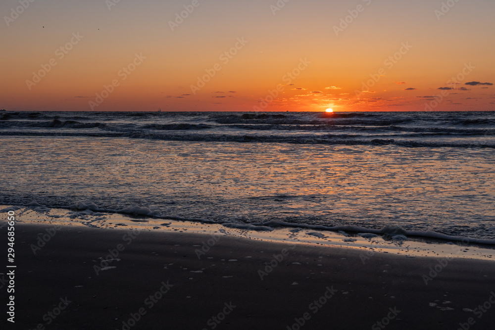 Beautiful sunset landscape at the North sea and orange sky above it with awesome sun golden reflection on waves as a background. Amazing summer sunset view on the beach.