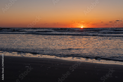 Beautiful sunset landscape at the North sea and orange sky above it with awesome sun golden reflection on waves as a background. Amazing summer sunset view on the beach.