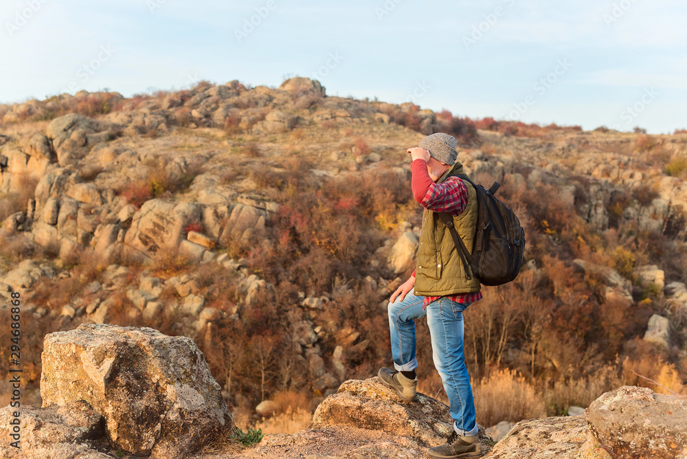 Fototapeta premium Elderly gray-haired tourist with a beard in plaid red shirt on the background of the gorge and stones