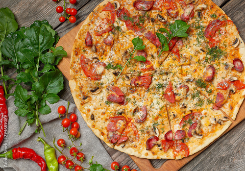 baked round pizza with smoked sausages, mushrooms, tomatoes, cheese and arugula leaves