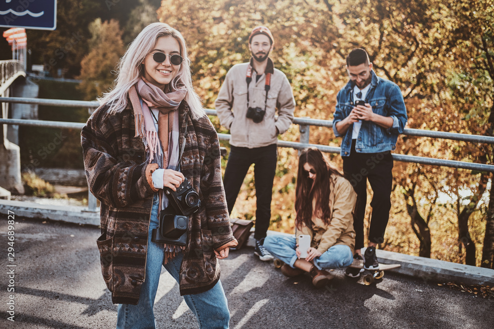 Attractive blond girl with photo camera is enjoying autumn walk with her friends. Attractive blond girl with photo camera is enjoying autumn walk with her friends.