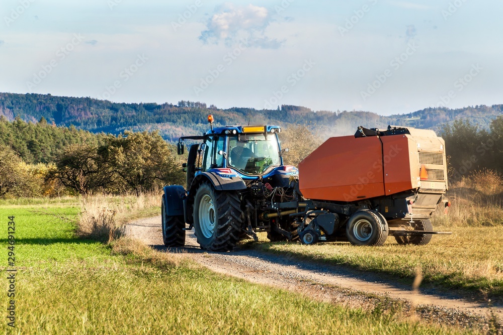 Obraz premium Blue tractor packs straw. Autumn work on the farm. Tractor on the field. Ecological agriculture.