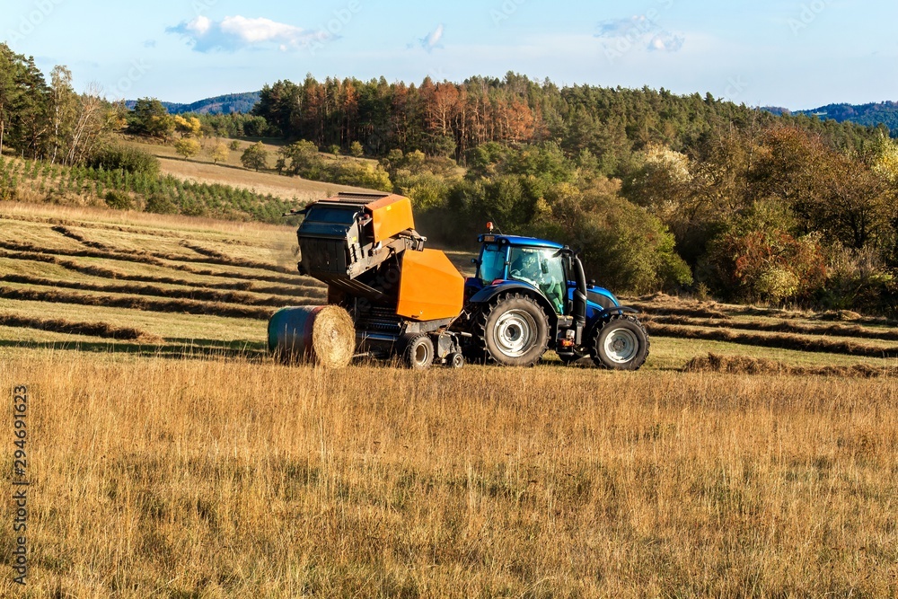 Fototapeta premium Blue tractor packs straw. Autumn work on the farm. Tractor on the field. Ecological agriculture.