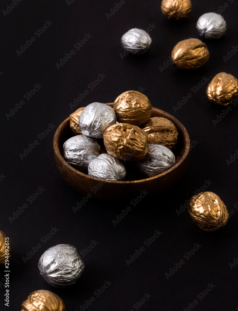 Obraz premium Painted golden and silver walnuts on wooden plate on black background