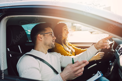 Driving school or test. Beautiful young pregnant woman learning how to drive car together with her instructor.