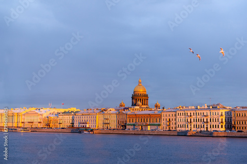 view of the Neva embankment from the river, buildings, the dome of St. Isaac's Cathedral, at sunset in the sun, birds in the sky