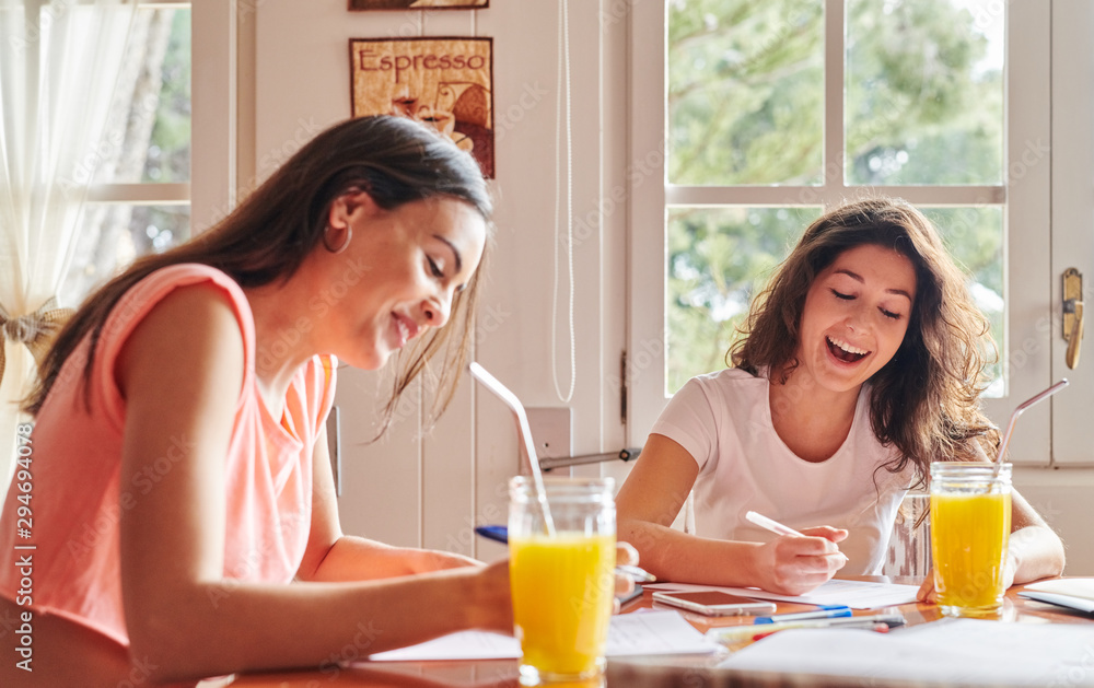 Laughing girls with drinks at table doing studies Laughing girls with drinks at table doing studies