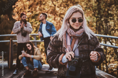 Smiling cheerful lady in sunglasses is posing for photographer while holding photo camera.