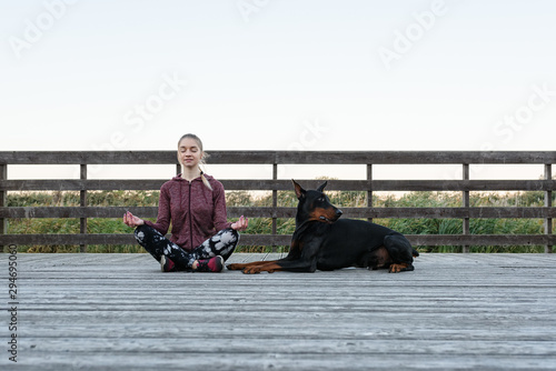 Girl meditating on pier with dog near photo