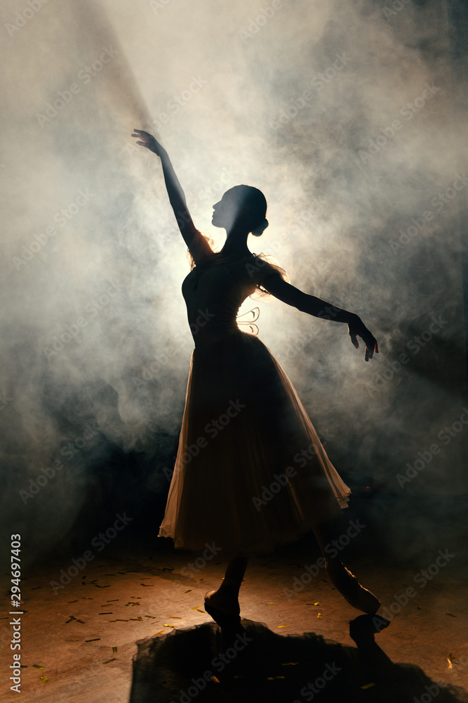 Ballerina in dress stretching on scene in darkness Ballerina in dress stretching on scene in darkness