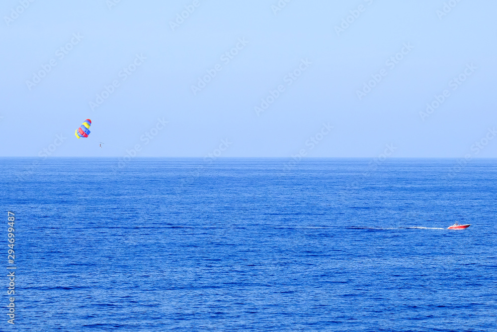 a man is flying on a parachute behind a boat over sea