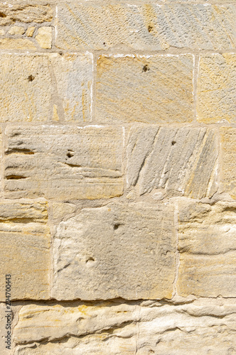 Fototapeta Naklejka Na Ścianę i Meble -  idyllische, schön restaurierte Sandsteinmauer eines historischen Gebäudes aus gelbem Sandstein mit verschiedener  Oberflächenstruktur, manche Steine haben Auswaschungen und Löcher, wie Schusslöcher