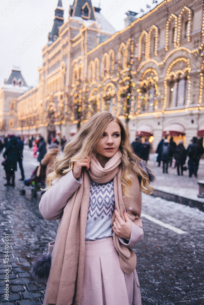 A young woman walks at Christmas in the square near the decorated Christmas trees. Candy is a lollipop in the form of a heart. A young woman walks at Christmas in the square near the decorated Christmas trees. Candy is a lollipop in the form of a heart.