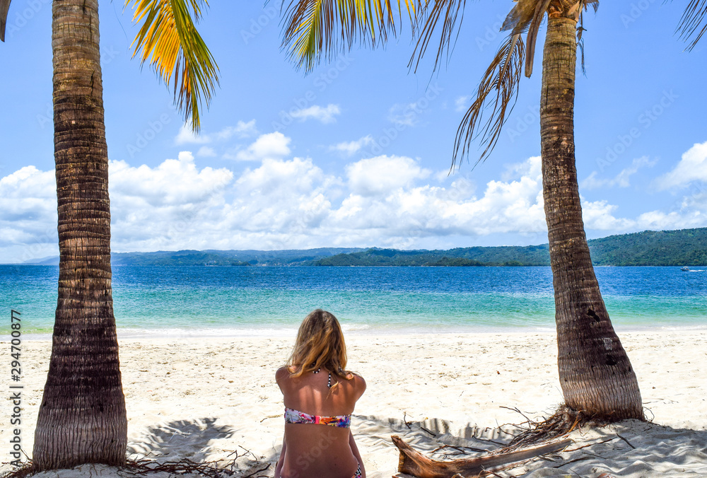 Woman sitting on white beach between two palms in front of beautiful ocean