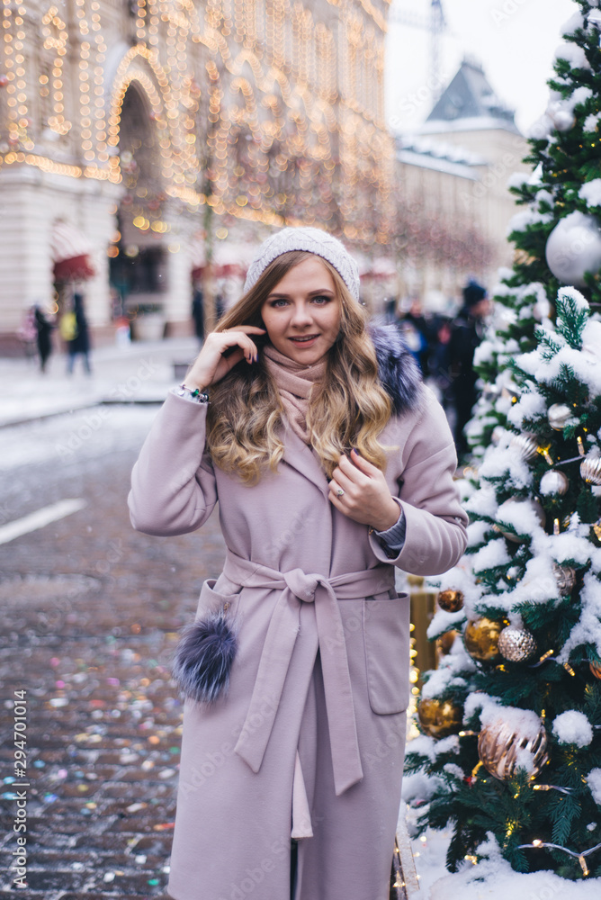 A young woman walks at Christmas in the square near the decorated Christmas trees. Candy is a lollipop in the form of a heart.