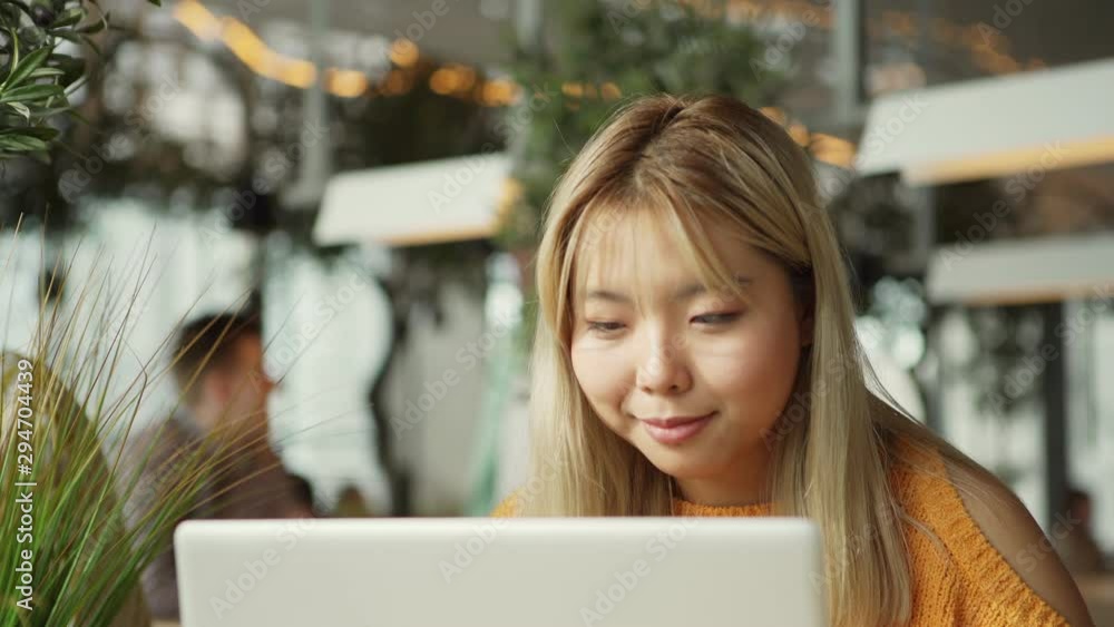 Young ethnic female smiling and browsing laptop while doing remote job in cozy cafe Young ethnic female smiling and browsing laptop while doing remote job in cozy cafe