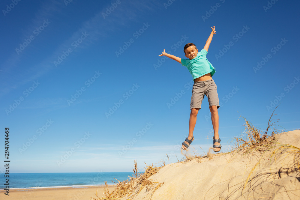 Cute boy jump on the sand dune beach raising hands Cute boy jump on the sand dune beach raising hands
