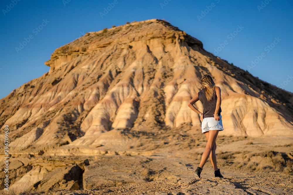 Lifestyle of a young blonde with rocker look with high shoes walking towards a hill in the desert of the Bardenas Reales