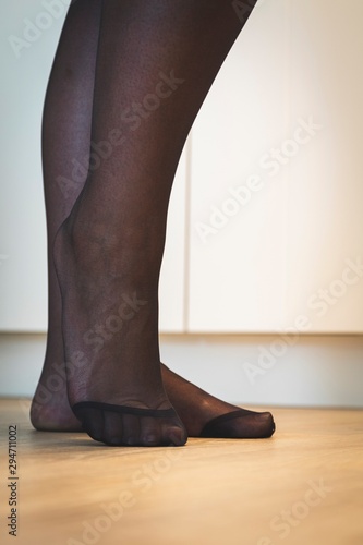 An elegant close up portrait of the feet of a girl in black pantyhose with the nylon at the toes being reinforced standing on a wooden floor and posing.