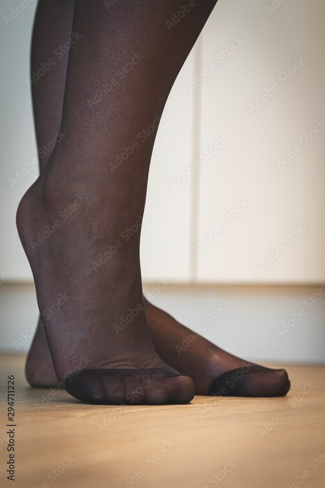 A close up portrait of the elegant feet of a girl in black pantyhose with  the nylon at the toes being reinforced standing on a wooden floor and  posing. Stock Photo