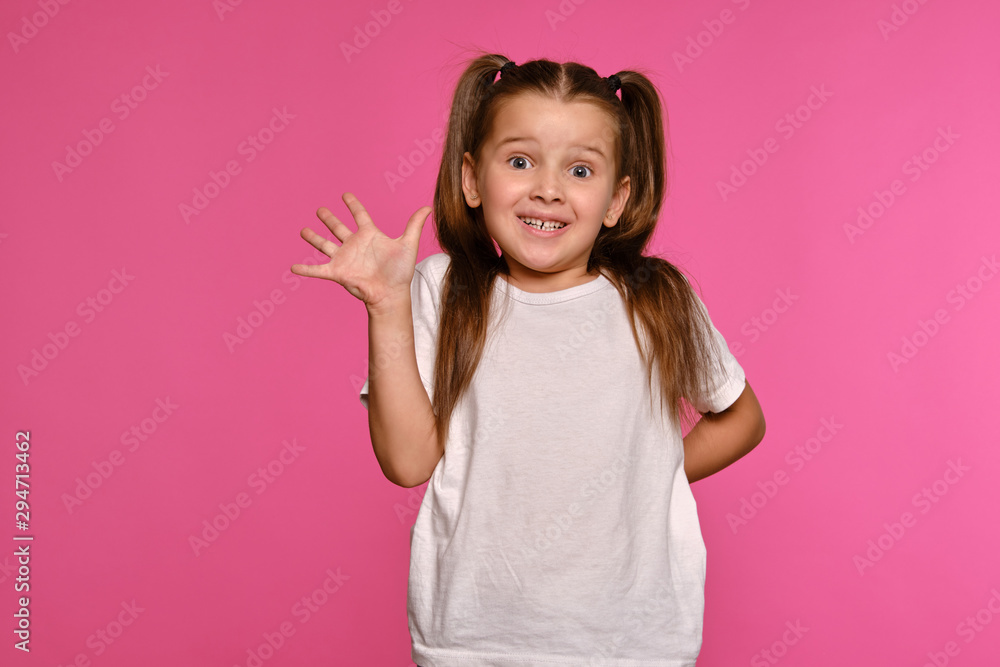 Little girl with ponytails, dressed in white t-shirt is posing against a pink studio background. Close-up shot. Sincere emotions. Little girl with ponytails, dressed in white t-shirt is posing against a pink studio background. Close-up shot. Sincere emotions.
