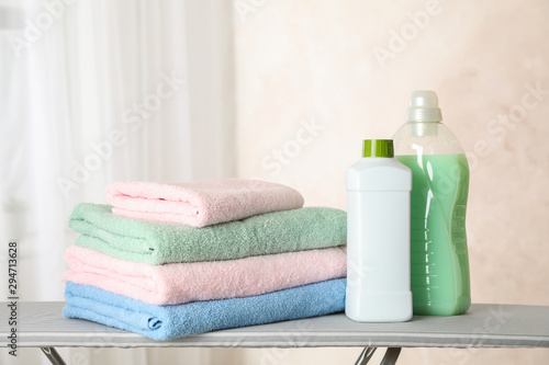 Stack of clean towels and laundry liquid on ironing board, copy space