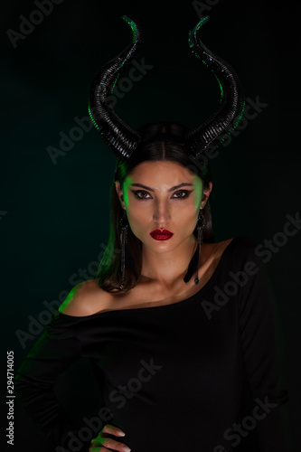 Concept of Halloween and fantasy horror. Cosplay on Maleficent demonic - starring. Face of beautiful woman from a fairytale with horns in green smoke. Beautiful girl dressed up as devil.
