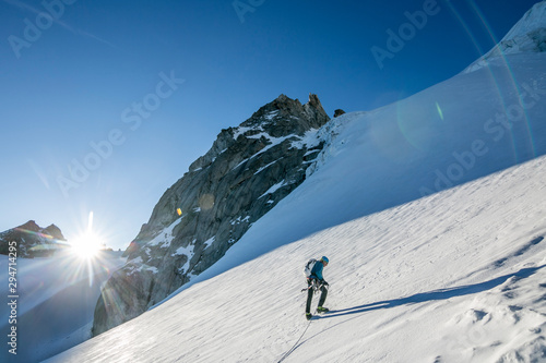 A climber starts up a steep snow slope as the sun crests the horizon photo