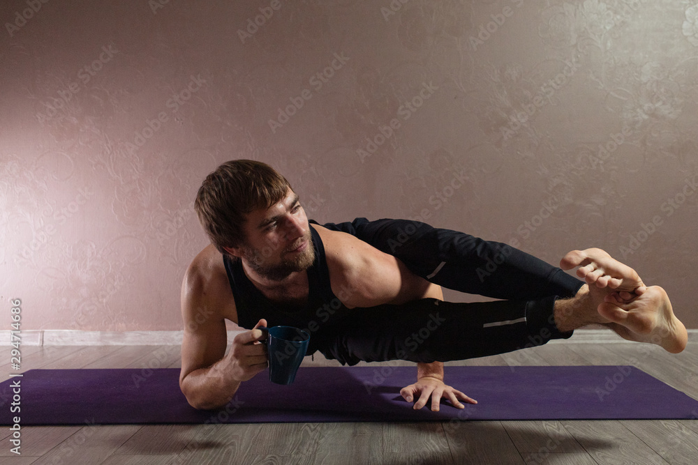 Young sporty man practicing yoga, meditating in yoga pose, working out, wearing sportswear, indoor full length, brown yoga studio
