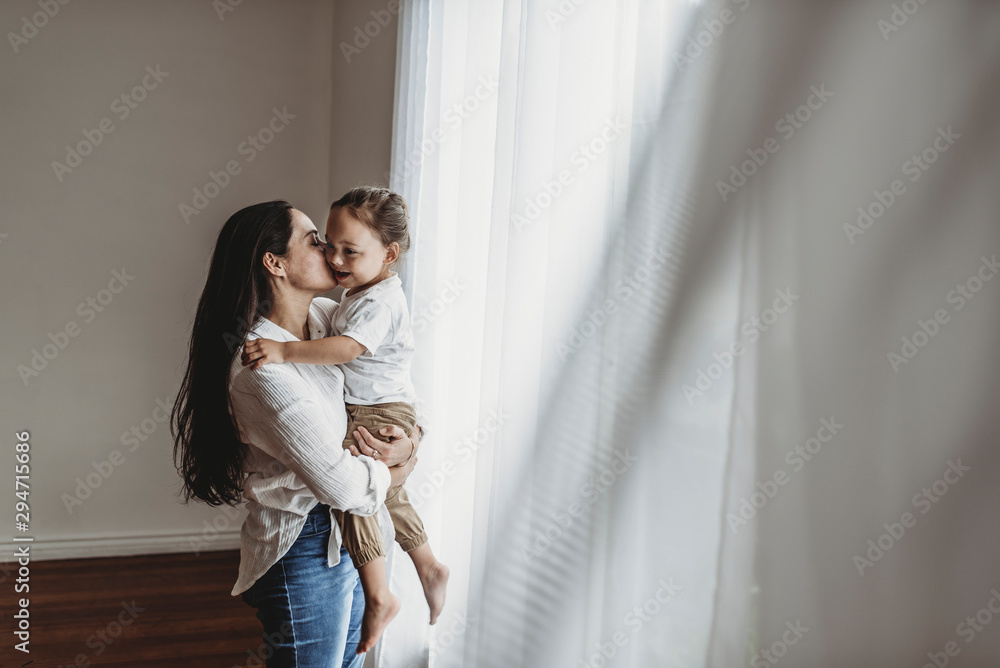 Side view of young mother holding toddler boy in embrace and kissing Side view of young mother holding toddler boy in embrace and kissing